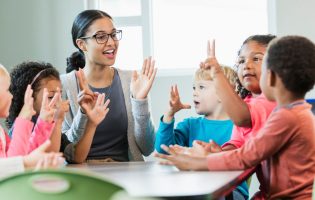 Première rentrée d'une jeune enseignante assise à une table entourée de jeune enfants