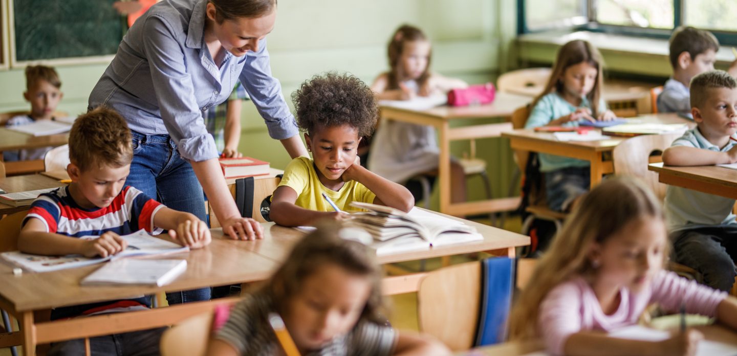 Salle de classe élémentaire, une jeune enseignante parle à un élève
