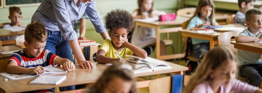 Salle de classe élémentaire, une jeune enseignante parle à un élève